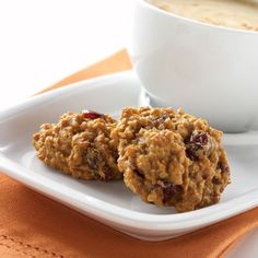 two oatmeal cookies on a white plate next to a cup of coffee