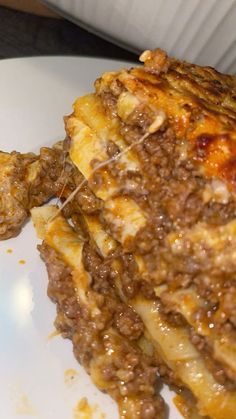 a white plate topped with lasagna covered in cheese and meat sauce next to a slice of pizza