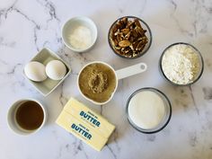 an assortment of ingredients are laid out on a marble counter top, including eggs, butter, and flour