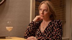 a woman sitting at a table with a glass of wine in front of her and looking off to the side