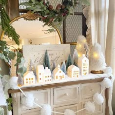 a white dresser topped with christmas decorations and lights next to a mirror in a room