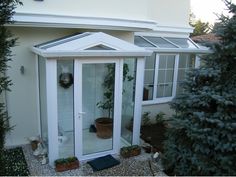 a small white building with a glass door and potted plants in the front yard