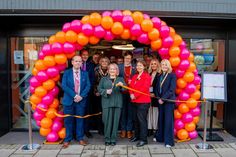 a group of people standing in front of a pink and orange arch with balloons on it