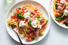 two plates of pasta with meat, cheese and spinach on the side next to a glass of water