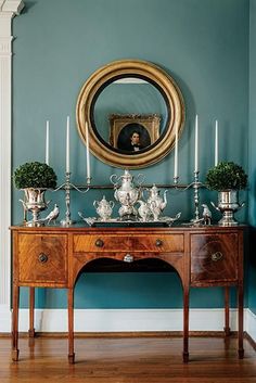 a table with candles, vases and an oval mirror on the wall above it