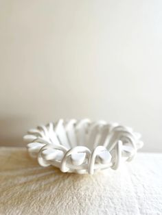 a white bowl sitting on top of a bed next to a wall and flooring