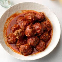 a white bowl filled with meatballs covered in marinara sauce on top of a table