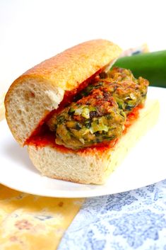 a close up of a sandwich on a plate near a green pickle leaf and table cloth