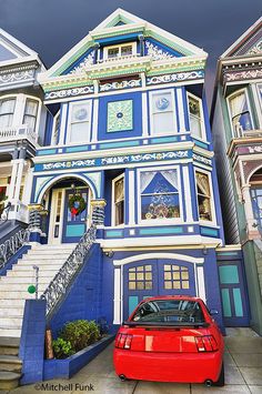 a red car is parked in front of a blue house with stairs and balconies