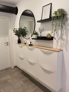 a white dresser with two mirrors and plants on the top shelf in front of it