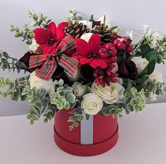 a red box with white flowers and greenery in it is sitting on a table