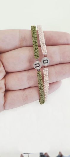 two bracelets with letters on them are held in someone's hand, one is green and the other is white