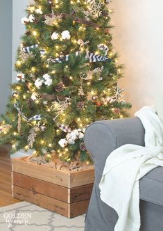 a small christmas tree with white lights in a wooden box on the floor next to a couch