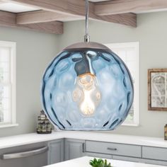 a light that is hanging from the ceiling in a kitchen with white counter tops and gray cabinets