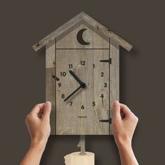 two hands are holding a wooden clock with the image of a house and moon on it