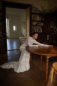 a woman is sitting at a table in a room with wooden floors and walls, looking off to the side