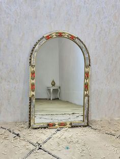 a mirror sitting on top of a floor next to a white table with a vase