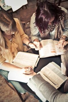 three women sitting at a table with open books