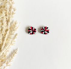 two black and red earrings sitting on top of a white surface next to a plant