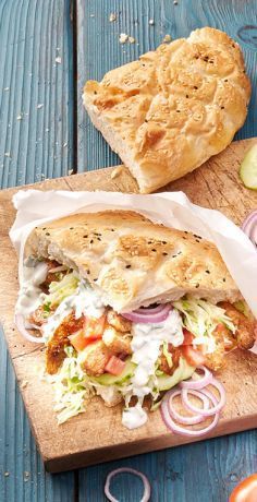 a sandwich on a wooden cutting board with onions, tomatoes and cucumbers next to it