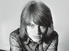 a black and white photo of a man with long hair wearing a shirt looking at the camera