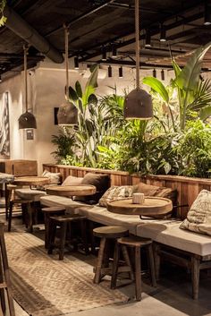 an outdoor restaurant with tables and stools, plants on the wall and hanging lamps