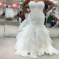 a woman standing in front of a mirror wearing a wedding dress with ruffles