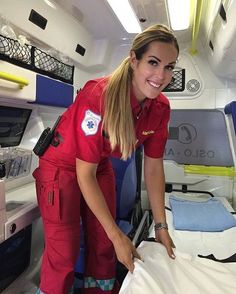 a woman in red uniform standing next to a bed with a white sheet on it