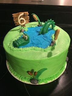 a birthday cake with green frosting and an alligator in the pond on top of it