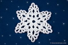 a crocheted snowflake sitting on top of a blue surface with stars in the background