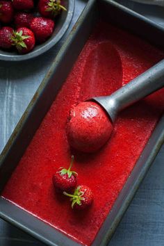 two strawberries sit on top of a red substance in a baking pan with a spatula