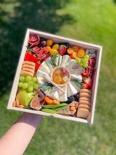 a hand holding up a box filled with assorted fruits and veggies on top of grass