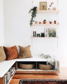 a white bench with pillows and plants on the shelf above it in a living room