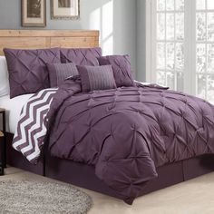 a bed with purple comforter and pillows on it