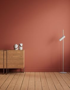 an empty room with red walls and two white vases on a wooden table next to a lamp