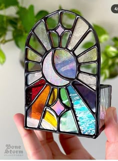 a hand holding up a stained glass sunburst in front of a potted plant