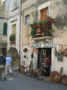 people are walking past an old building with flowers on the windows and plants in pots