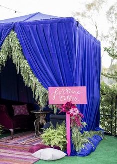 a blue tent with purple drapes and flowers on the ground in front of it