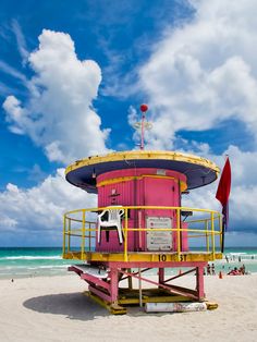 a lifeguard tower on the beach with people in the water and clouds above it