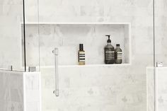 a bathroom with white marble walls and flooring, two soap dispensers on the shelf