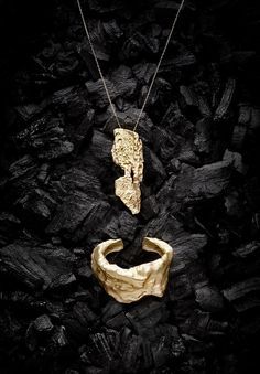 a gold necklace and ring sitting on top of some black rocks with one piece of jewelry in the middle