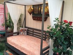 a canopy bed sitting on top of a wooden floor next to potted plants and flowers