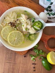 a bowl of soup with lemons, celery and noodles on a wooden cutting board