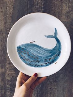 a hand holding a white plate with a blue whale painted on it