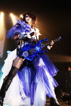 a woman dressed in blue and white holding a guitar while standing on top of a stage