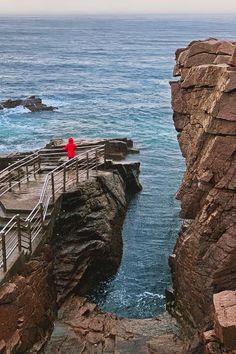 a person in red is standing at the edge of a cliff by the ocean with an umbrella over their head