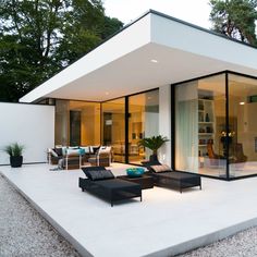 a modern house with glass walls and lots of furniture on the outside, in front of trees