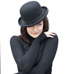 a woman wearing a black hat and sweater posing for the camera with her hand on her shoulder