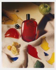 a red bottle sitting on top of a table next to fruit and other items in front of it