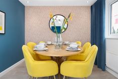 a dining room table with yellow chairs and plates on it, in front of a blue wall